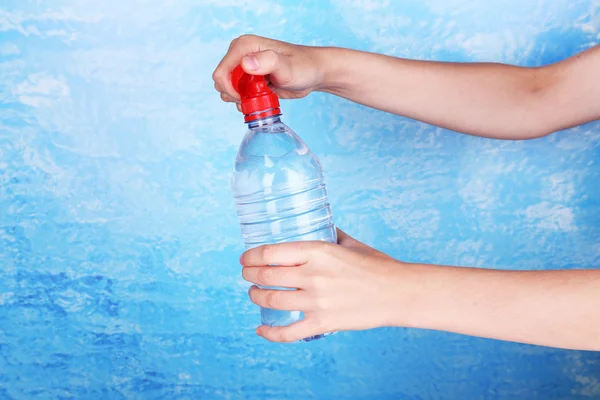 Main tient bouteille avec de l'eau sur fond bleu — Photo