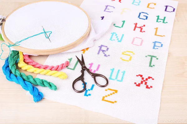 Handmade embroidered letters on white fabric and scissors on wooden background — Stock Photo, Image