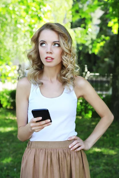 Beautiful young girl with mobile phone on city street — Stock Photo, Image