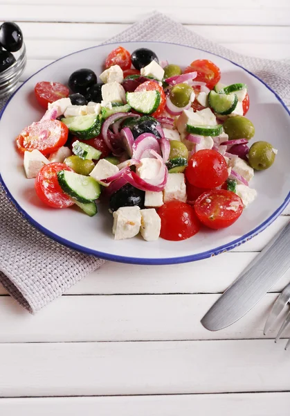 Greek salad served in plate on napkin on wooden background — Stock Photo, Image