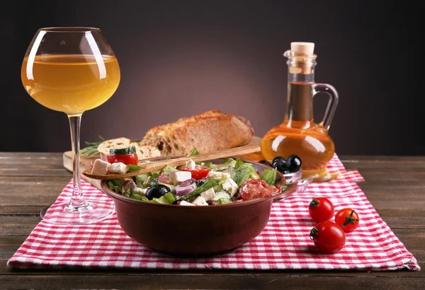 Schüssel mit griechischem Salat serviert mit Olivenöl und einem Glas Wein auf Serviette auf einem Holztisch vor dunklem Hintergrund — Stockfoto