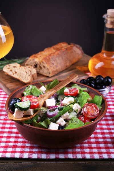 Skål med grekisk sallad serveras med olivolja och glas vin på servett på träbord på mörk bakgrund — Stockfoto