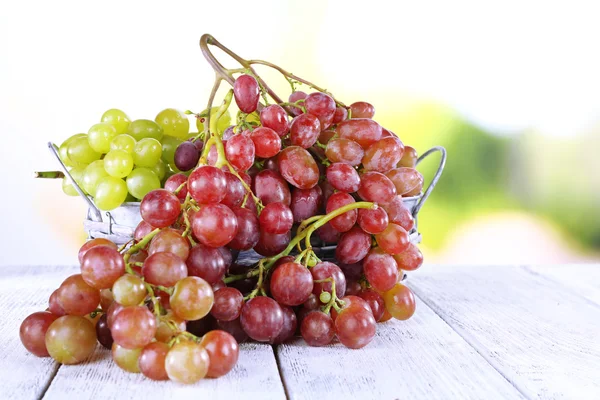 Bunches of ripe grape in wicker basket on wooden table on natural background — Stock Photo, Image