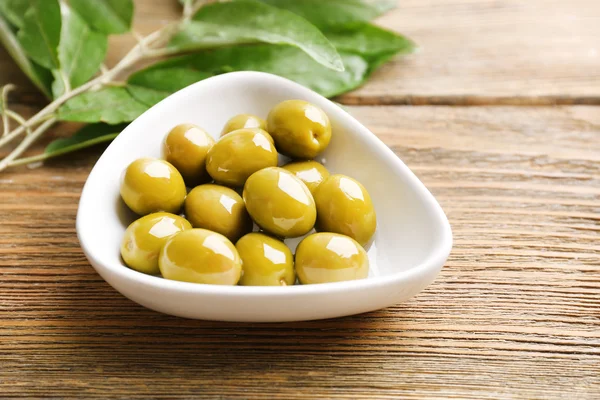 Зеленые оливки в миске с листьями на столе крупным планом — стоковое фото