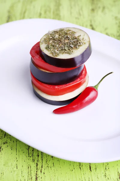 Slices of aubergines with tomatoes and chilly pepper on plate on wooden background — Stock Photo, Image