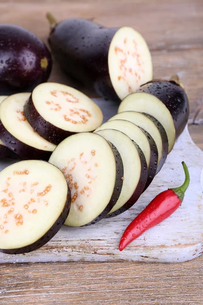 Chopped aubergines with chilly pepper on cutting board on wooden background — Stock Photo, Image