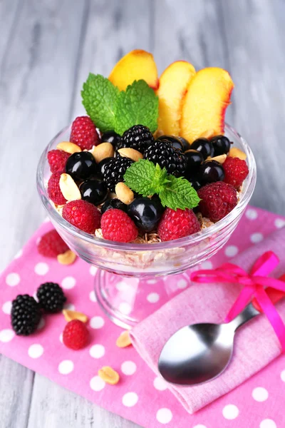 Petit déjeuner sain - yaourt aux fruits frais, baies et muesli servi dans un bol en verre sur fond de bois de couleur — Photo