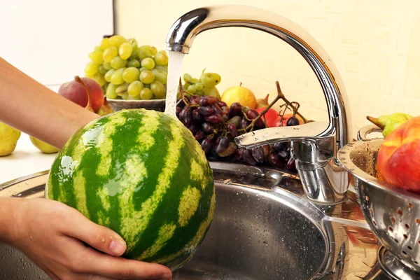 Woman's hands washing watermelon and other fruits in colander in sink — Stock Photo, Image