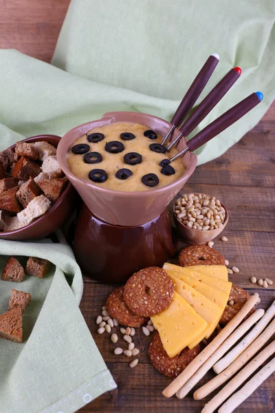 Fondue, olives, slices of cheese, rusks and spices on napkin on wooden background — Stock Photo, Image