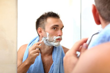 Genç adam banyoda sakalını kesiyor.