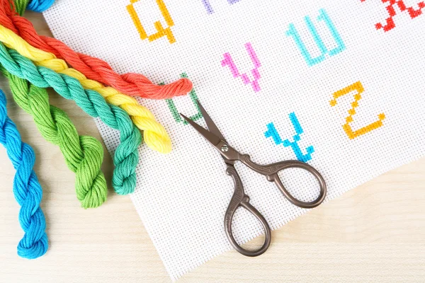 Handmade embroidered letters on white fabric and scissors on wooden background — Stock Photo, Image