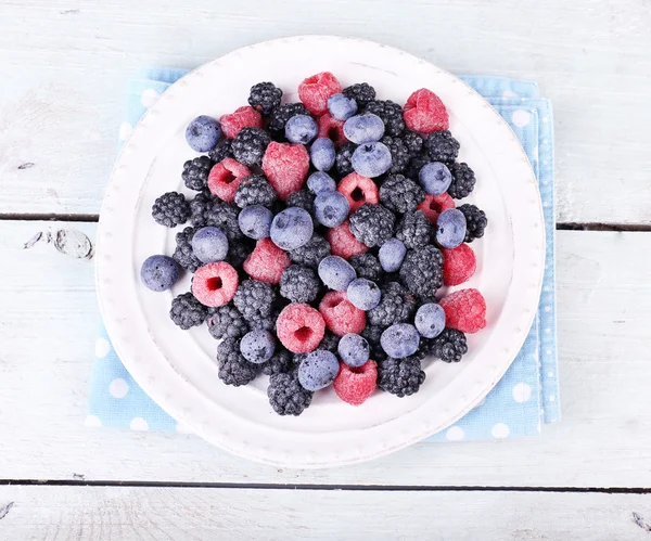 Geeiste Beeren auf Teller, auf farbigem Holzhintergrund — Stockfoto