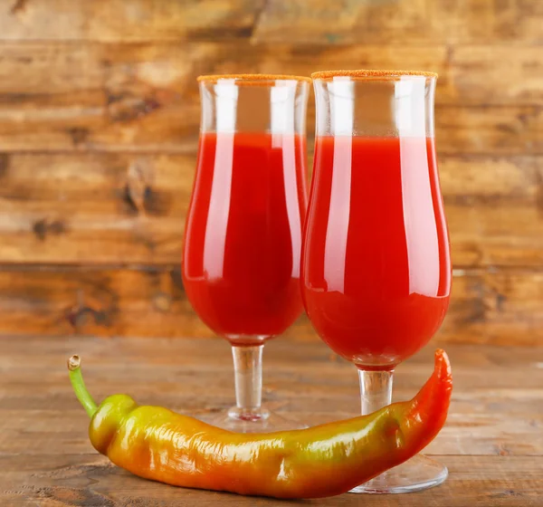 Стаканы вкусного томатного сока и перца на деревянном столе — стоковое фото