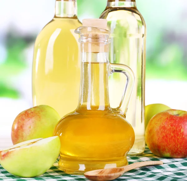 苹果醋玻璃瓶和成熟的新鲜苹果，木制的桌子，对自然背景上 — 图库照片