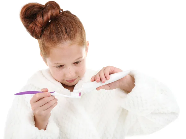 Menina bonita em roupão de banho segurando escova de dentes e pasta de dentes isolada no branco — Fotografia de Stock