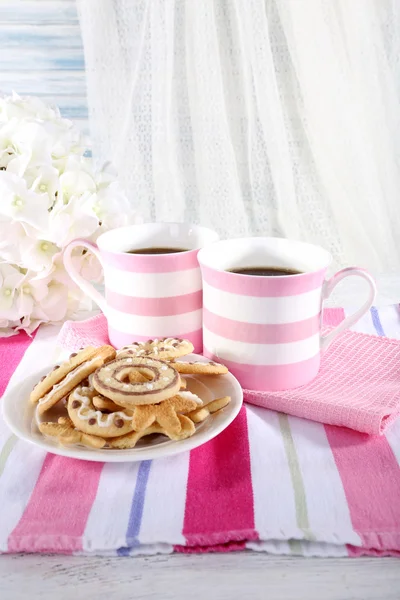 Two mugs of coffee with biscuits on napkin on table on white curtain background — Stock Photo, Image