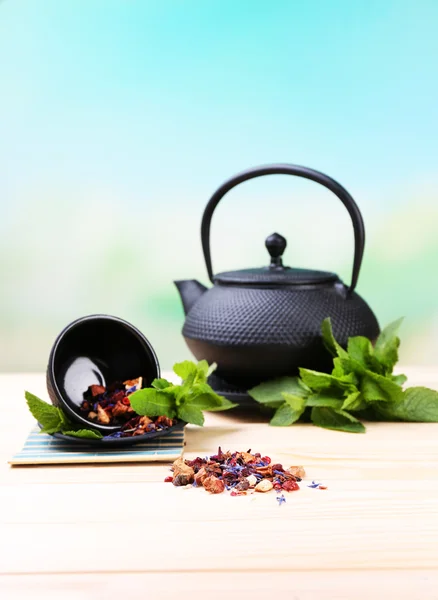 Chinese traditional teapot with fresh mint leaves and dried hibiscus petals on wooden table, on bright background — Stock Photo, Image