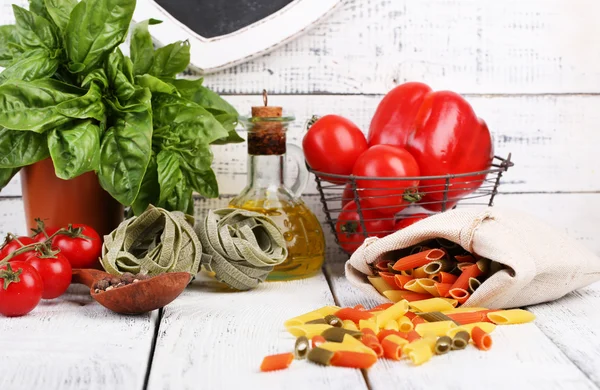 Zusammensetzung aus bunten Nudeln, frischen Tomaten, Basilikum, Olivenöl in der Flasche auf Holzgrund — Stockfoto