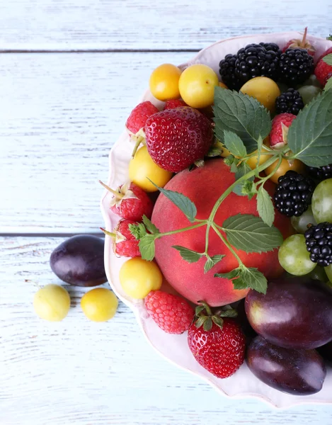 Различные ягоды и фрукты в тарелке на деревянном столе крупным планом — стоковое фото