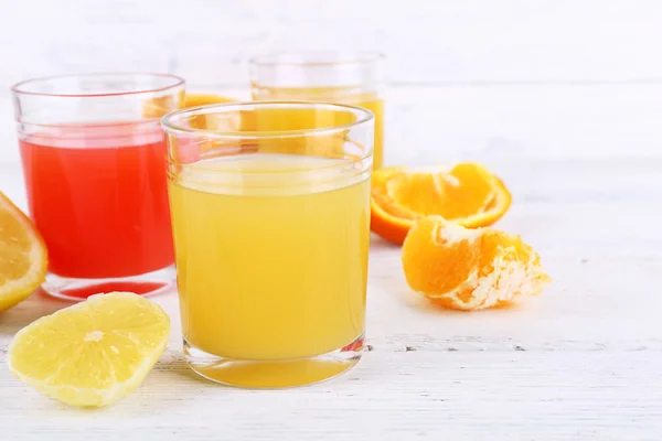 Olika skivade citrusfrukter och glas juice på träbord — Stockfoto