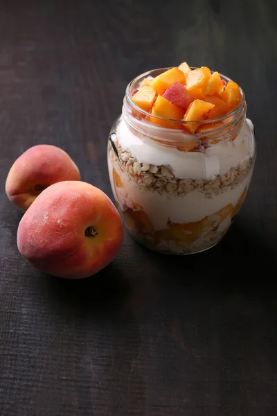 Healthy breakfast - yogurt with  fresh peach and muesli served in glass jar, on wooden background — Stock Photo, Image