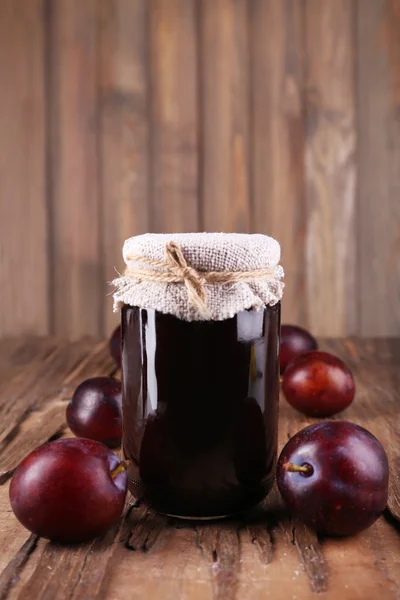 Tasty plum jam in jar and plums on wooden table close-up — Stock Photo, Image