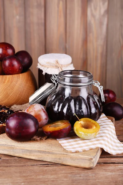 Tasty plum jam in jars and plums on wooden table on wooden background — Stock Photo, Image