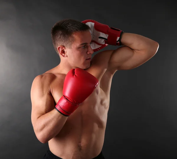 Schöner junger muskulöser Sportler mit Boxhandschuhen auf dunklem Hintergrund — Stockfoto