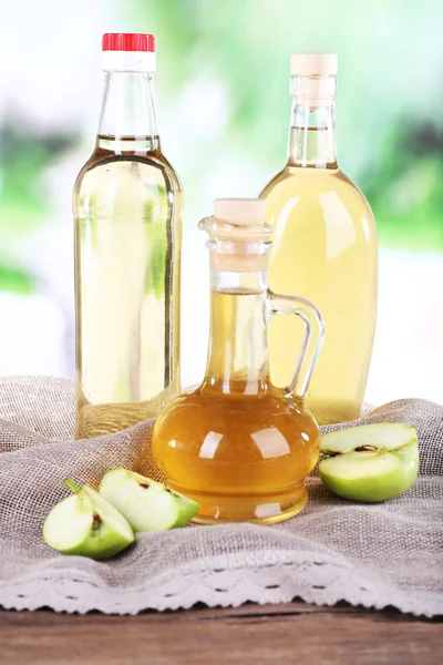 Apple cider vinegar in glass bottles and ripe fresh apples, on wooden table, on nature background — Stock Photo, Image