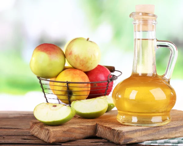 Äppelcidervinäger i glasflaska och mogna färska äpplen, på träbord, på natur bakgrund — Stockfoto