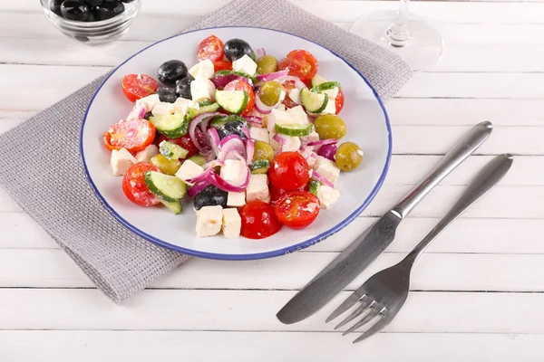 Greek salad served in plate on napkin on wooden background — Stock Photo, Image