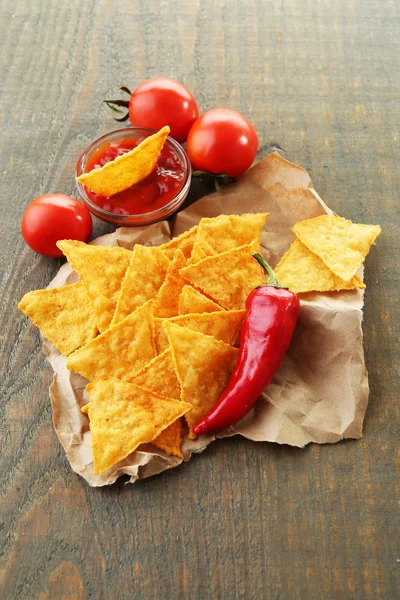 Leckere Nachos, rote Tomaten und Chilischoten auf Papier, auf Holzgrund — Stockfoto