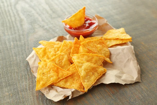 Välsmakande nachos och skål med sås på papper, på trä bakgrund — Stockfoto