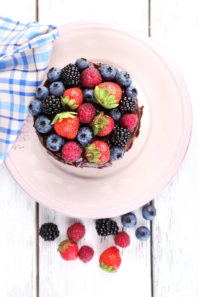 Smakelijke chocolate cake met verschillende bessen, op houten tafel — Stockfoto