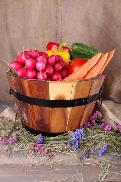 Gran canasta redonda de madera con verduras sobre fondo de saco — Foto de Stock