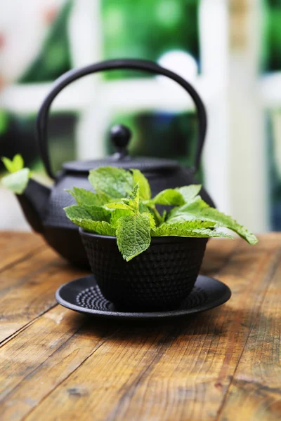 Teko Cina tradisional dengan daun mint segar di atas meja kayu, dengan latar belakang cerah — Stok Foto