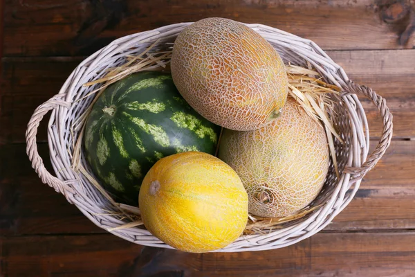 Meloner och vattenmelon i oval rotting korg på trä bakgrund — Stockfoto