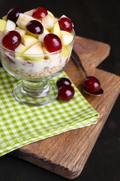 Здоровый завтрак - йогурт со свежим виноградом и яблочными ломтиками и мюсли подается в стеклянной миске, на деревянном фоне — стоковое фото
