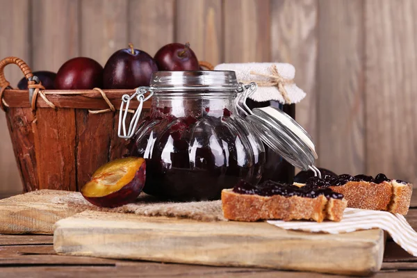 Tasty plum jam in jars and plums on wooden table on wooden background — Stock Photo, Image