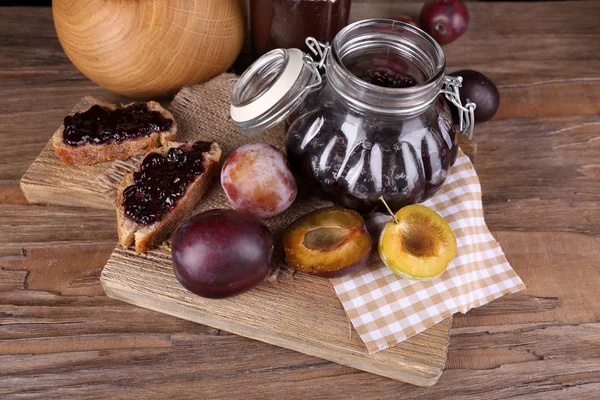 Tasty plum jam in jars and plums on wooden table close-up — Stock Photo, Image