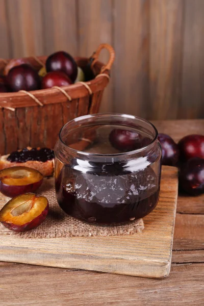 Engarrafamento de ameixa saboroso em jarro e ameixas em mesa de madeira em fundo de madeira — Fotografia de Stock