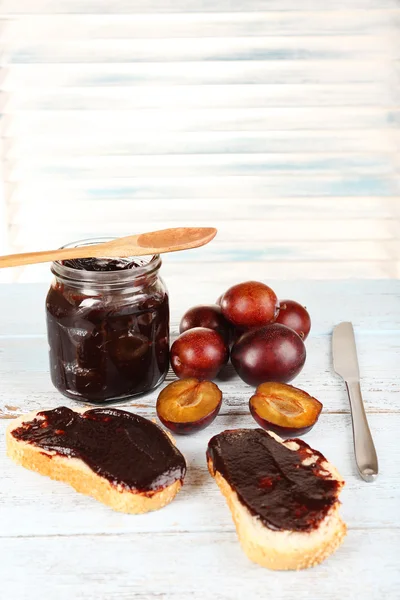 Bread with plum jam and plums on wooden table — Stock Photo, Image