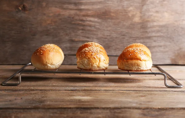 Tasty buns with sesame on oven-tray, on wooden background — Stock Photo, Image