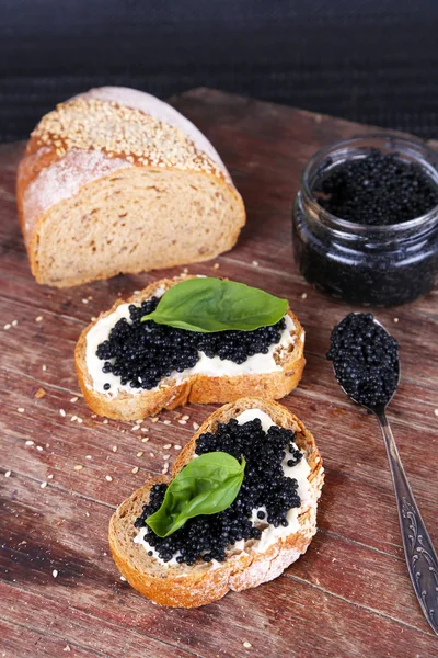 Skivor bröd med smör och svart kaviar på trä bakgrund — Stockfoto