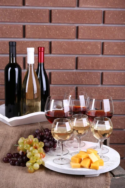 Botellas y vasos de vino, queso y uvas maduras en la mesa sobre fondo de pared de ladrillo —  Fotos de Stock
