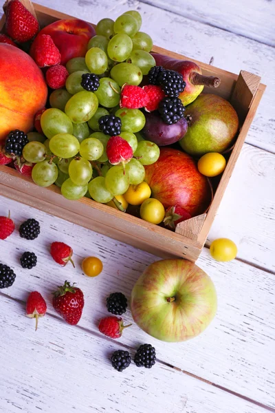 Diferentes bayas y frutas en caja sobre mesa de madera de primer plano — Foto de Stock