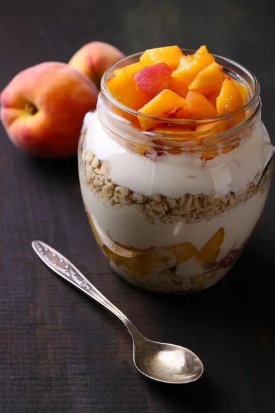 Colazione sana - yogurt con pesca fresca e muesli servito in barattolo di vetro, su sfondo di legno — Foto Stock