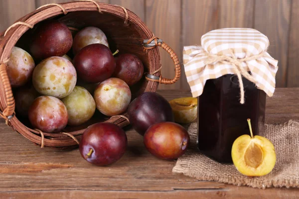Confiture de prunes savoureuse en pot et prunes sur table en bois sur fond en bois — Photo