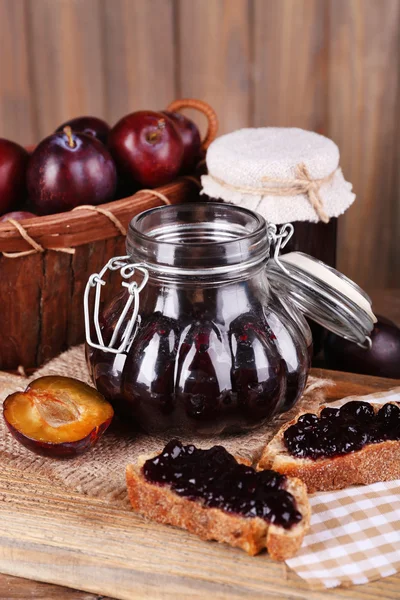 Tasty plum jam in jars and plums on wooden table on wooden background — Stock Photo, Image