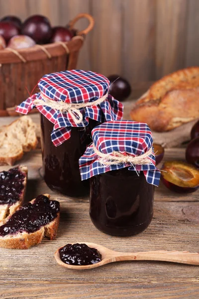 Confiture de prunes savoureuse dans des pots et des prunes sur une table en bois — Photo